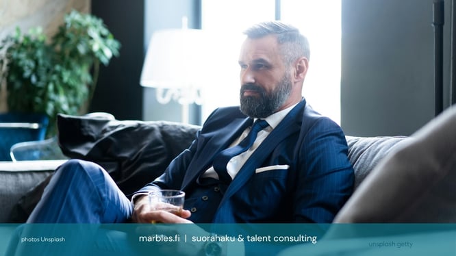 Haastateltava kandi istuu rauhallisesti tummalla sohvalla | Marbles