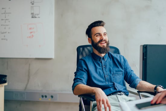 Nuori parrakas mies istuu toimistolla ja hymyilee